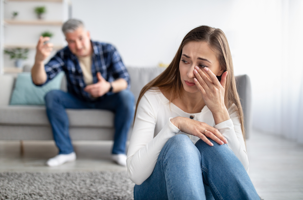 Emotional or psychological domestic violence concept. Mature man abusing his depressed wife, shouting, humiliating and threatening her, middle aged woman crying on floor at home