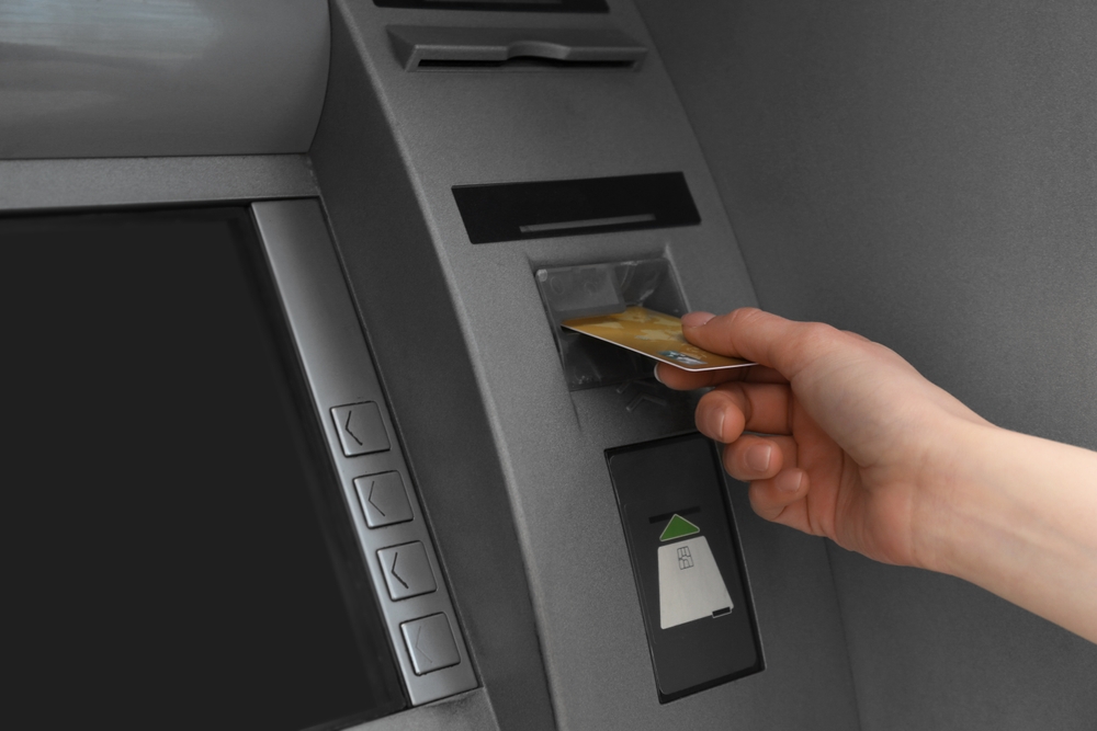 Woman inserting credit card into cash machine outdoors, closeup