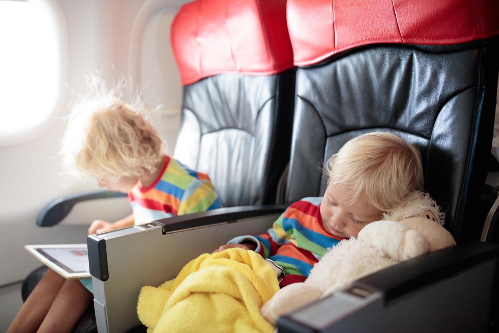 Child in airplane. Kid in air plane sitting in window seat. Flight entertainment for kids. Traveling with young children. Kids fly and travel. Family summer vacation. Little boy with toy in airplane.