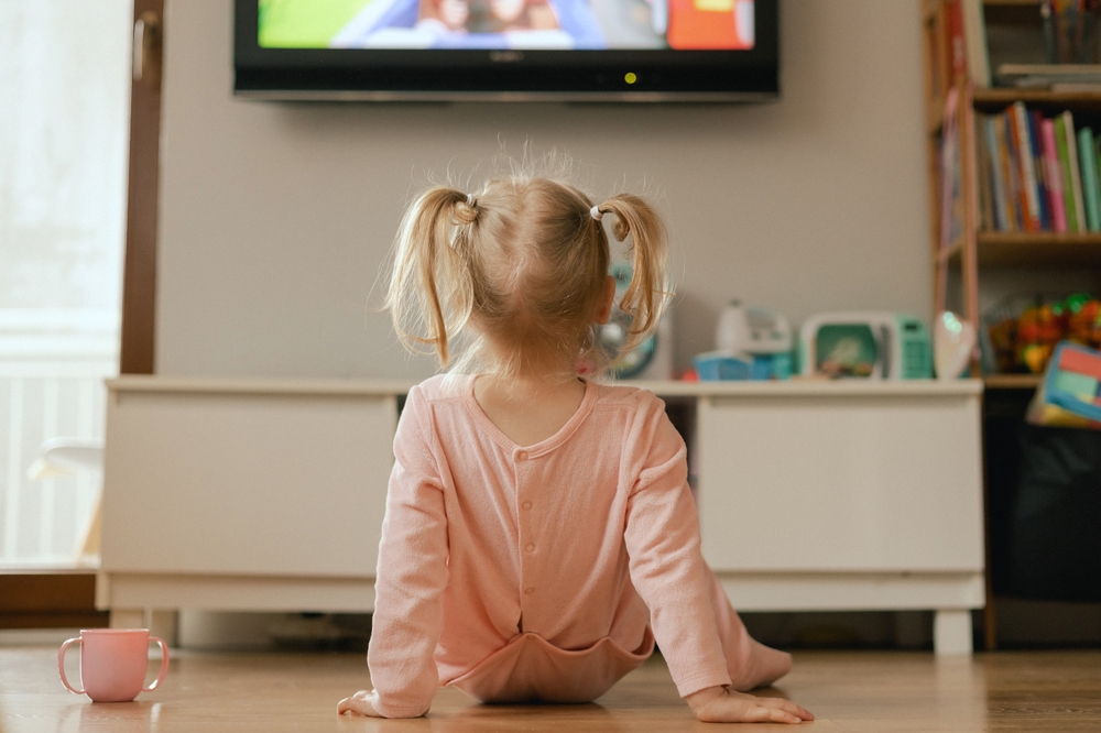 Portrait of happy baby playing with toys and watches cartoons on TV in playroom. Children and technology concept. Alpha Generation and modern technology with electronic device. Part of the series.