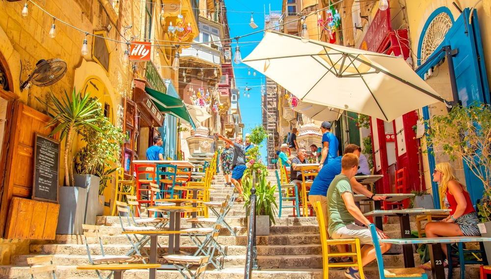 Valletta, Malta - 2 May, 2024: Wide panoramic view of summer street and pavement cafe in Valletta old town. Beautiful Maltese travel photo with colorful urban life.