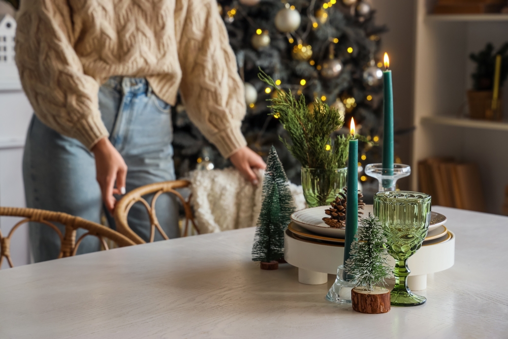 Burning candles with Christmas decor on dining table against woman at home, closeup