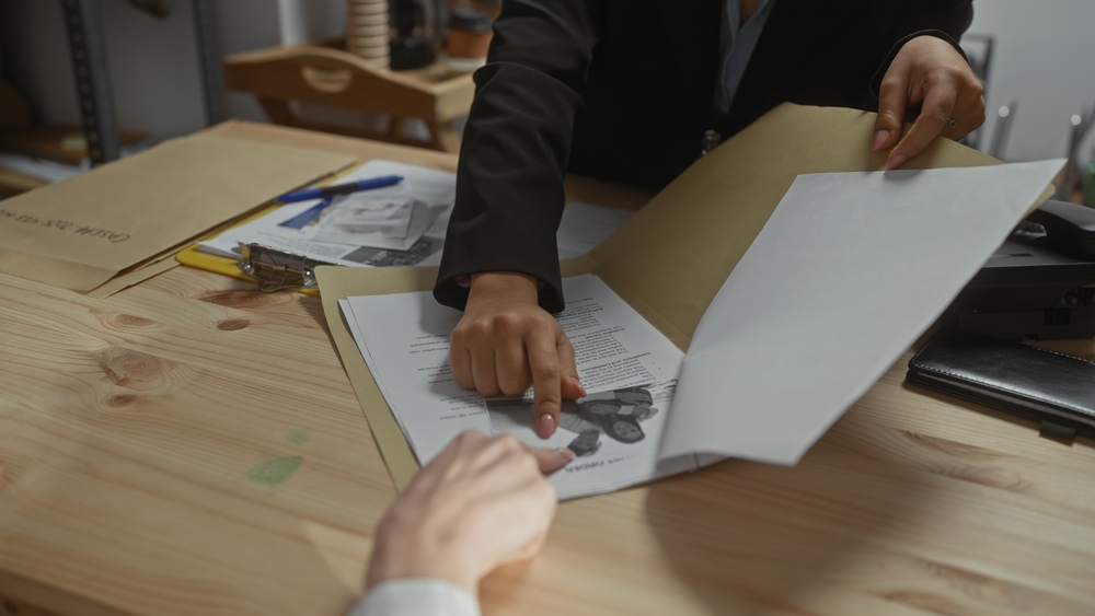 Two women in a police station inspect documents and evidence for an investigation.