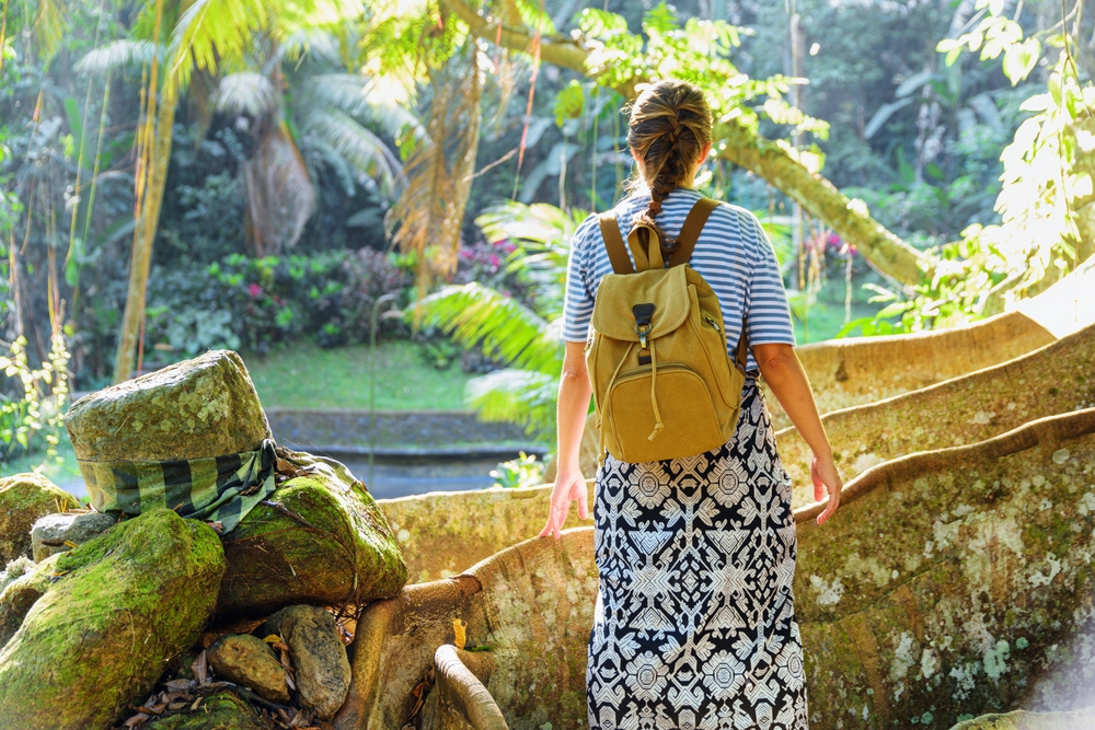 Female tourist with backpack enjoying view of a tropical forest. Woman staying among giant roots. Awesome fairy landscape. Amazing Asian trip. Solo traveler.