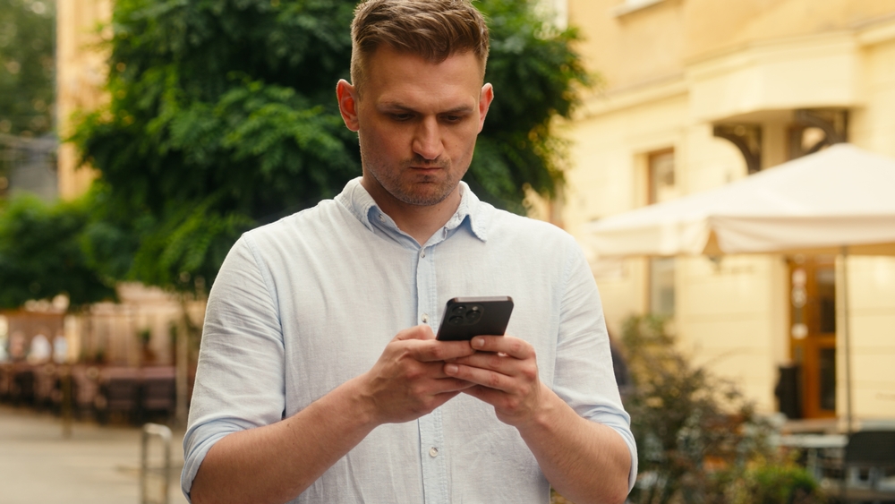 Angry Caucasian man typing texting message outdoors male mad anger irritated business guy businessman tourist customer smartphone chatting problem stress trouble displeased using mobile phone in city