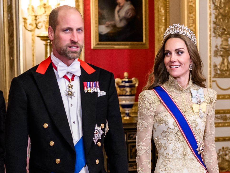 Prince William in formal evening dress with medals and Kate in a gold lace gown, blue sash, and diamond tiara standing in an ornate palace room.