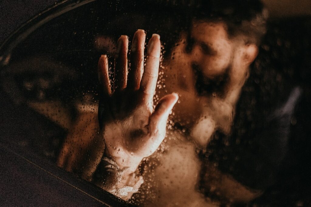 An intimate, moody shot of a couple behind steamy glass, with one hand pressed against the wet surface.