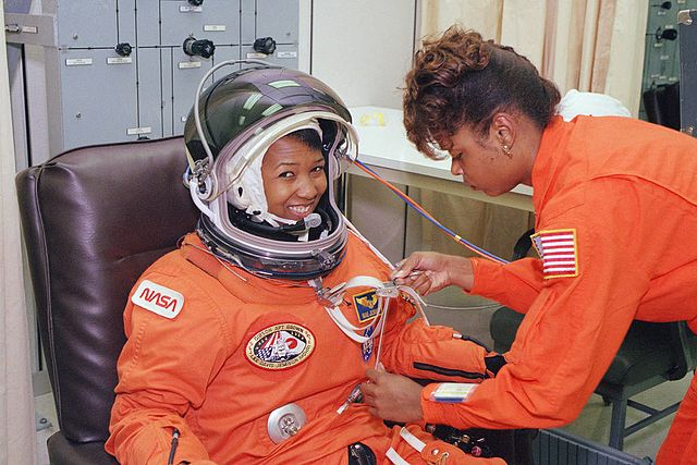 NASA astronaut Mae Jemison waits as her suit technician, Sharon McDougle, performs a leak check on her spacesuit
