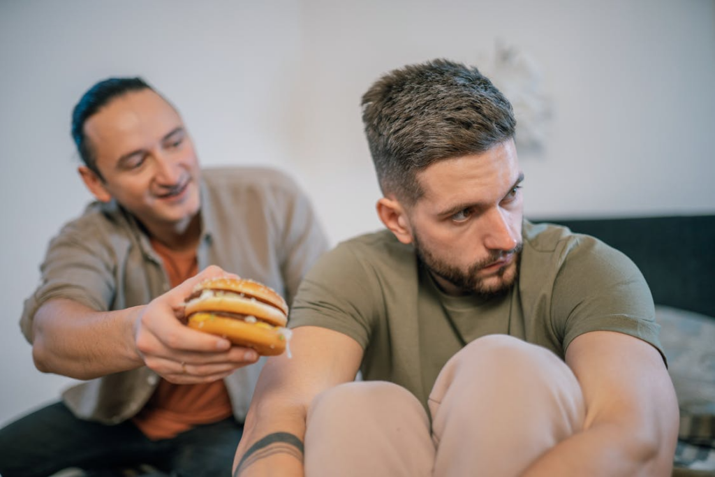 A Man Handing Burger to the Man Sitting Near Him
