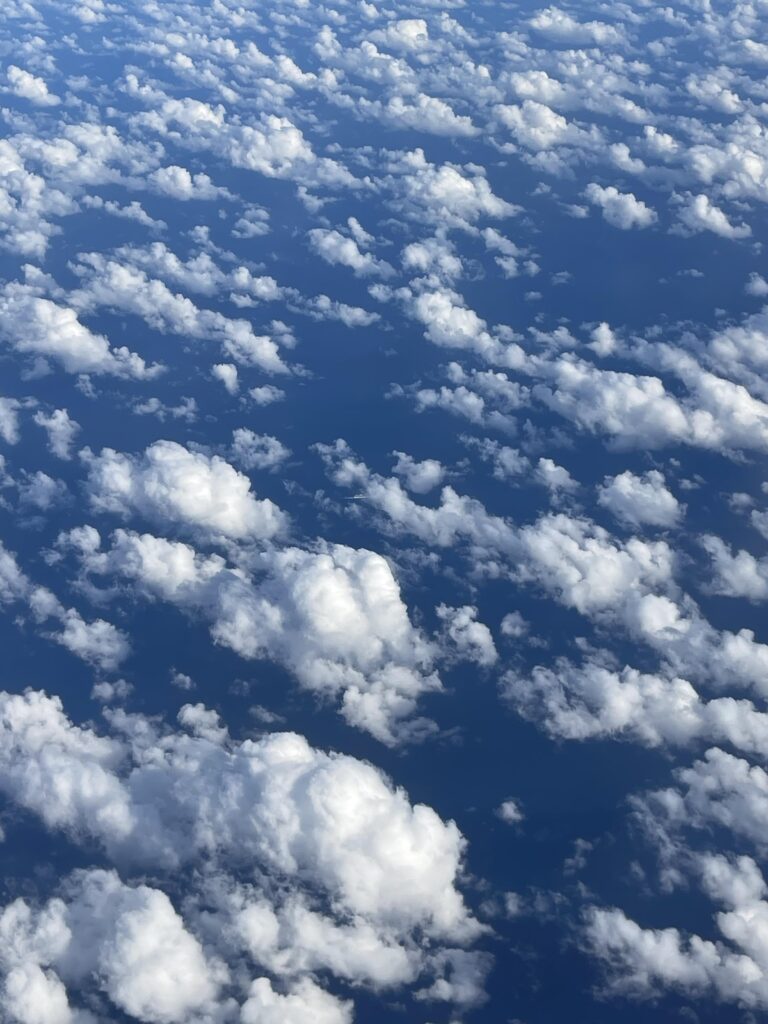 fluffy white clouds over the ocean in an image taken from an airplane window