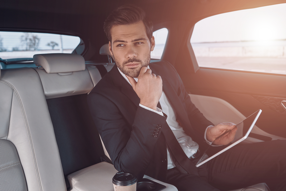 Young perfectionist. Handsome young man in full suit working using digital tablet while sitting in the car