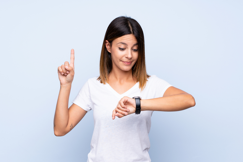 Young woman over isolated blue background looking at the hand watch