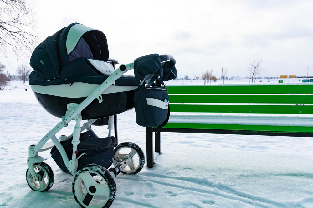 The child sleeps in a stroller. A baby stroller stands in the park by the bench in winter. frozen out