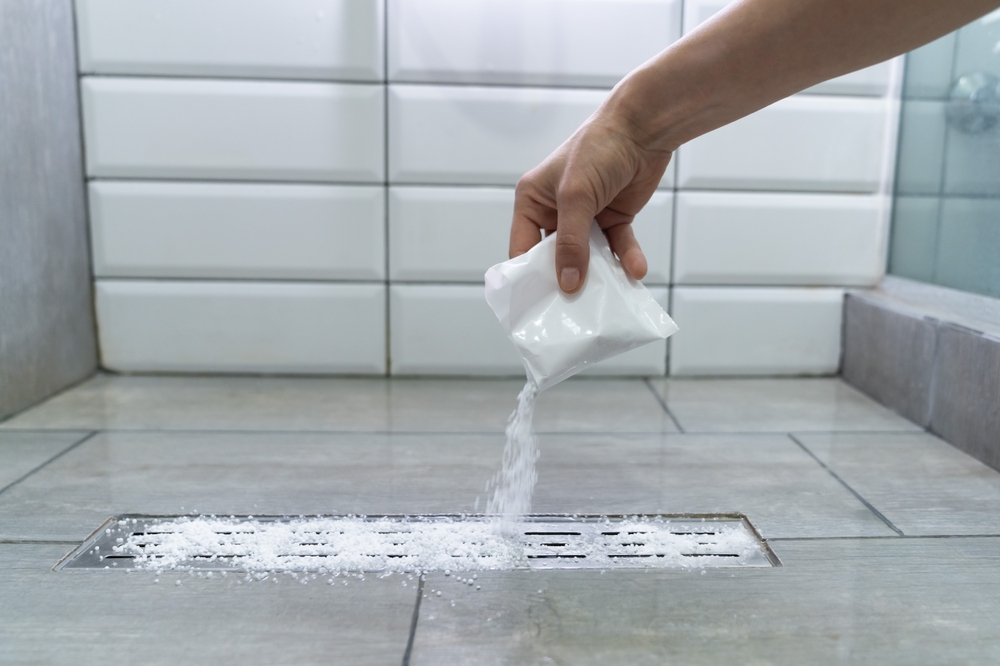 Closeup of woman hand pouring pipe cleaner granules. Removal of blockage in the shower of a special remedy with powder. Clean the blockages in the bathroom with chemicals.