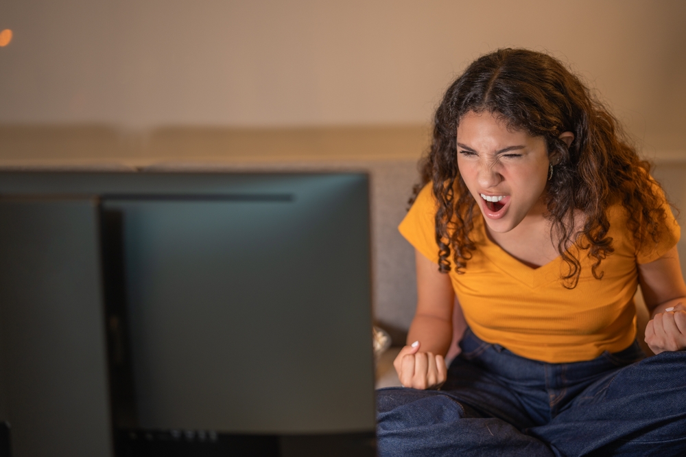 Young woman sitting screaming watching a movie on the TV in the living room of her apartment.