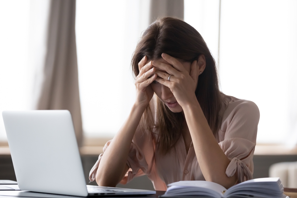 Frustrated stressed woman sit at desk near laptop hold head with hands feels desperate about dismissal, received bad news from bank business e-mail, personal life troubles, overworked headache concept
