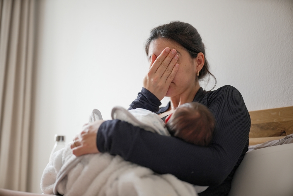 Mother breastfeeding her newborn baby while showing signs of exhaustion, highlighting the challenges and dedication involved in parenting.
