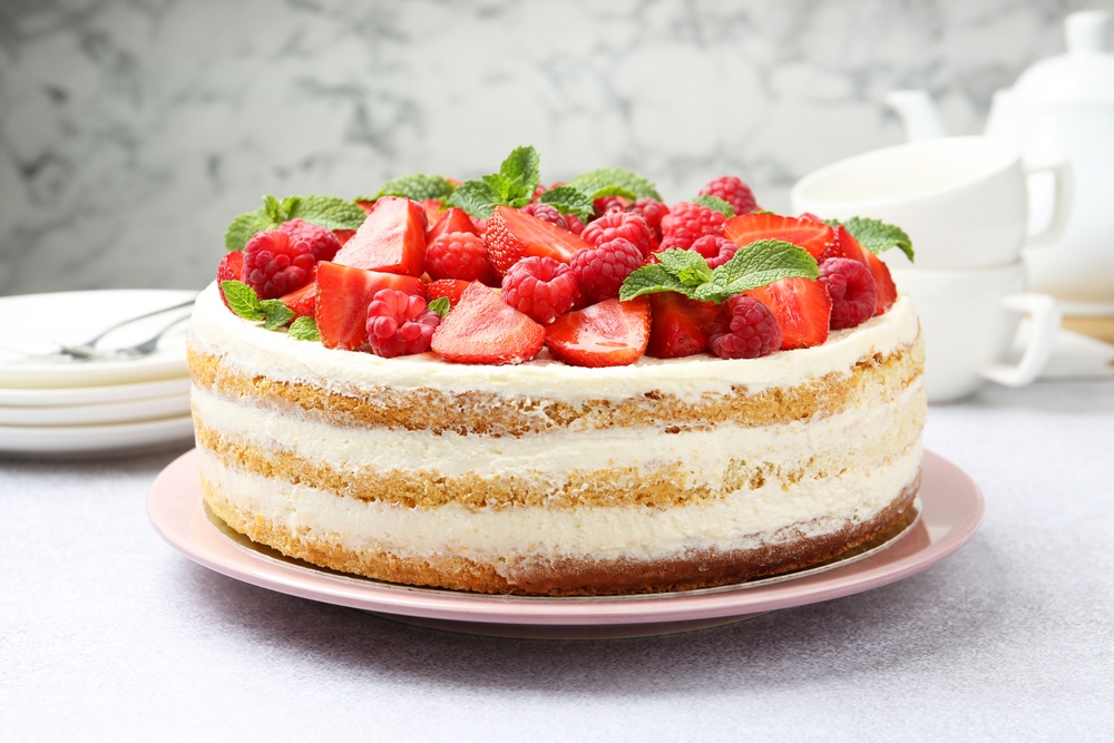 Tasty sponge cake with fresh berries and mint on light gray table