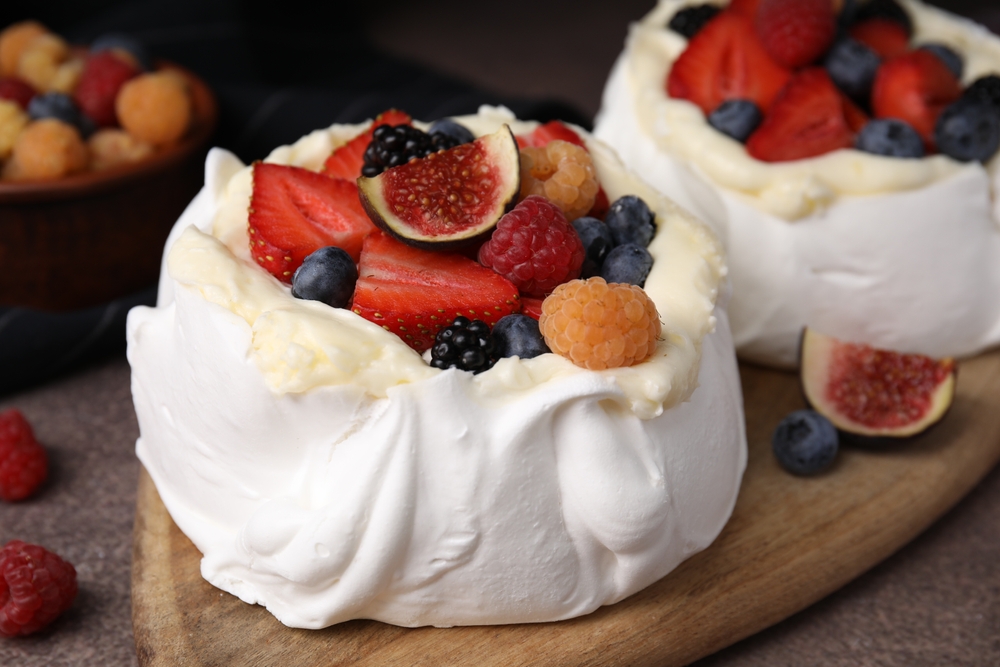 Pavlova cake (meringue dessert) with whipped cream, fresh berries and fig on brown table, closeup