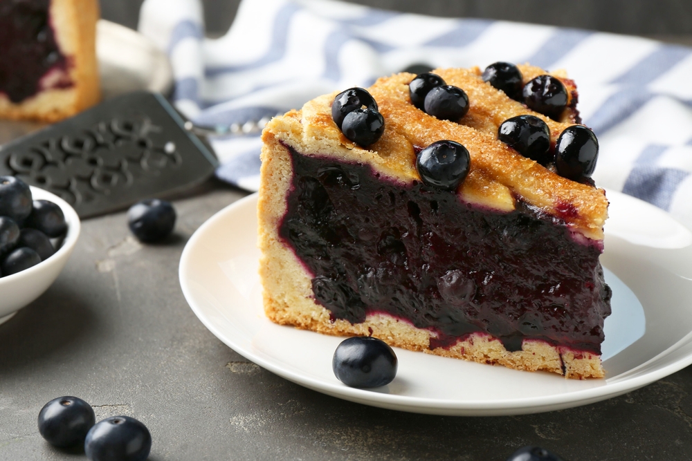 Slice of delicious homemade blueberry pie served on grey table, closeup