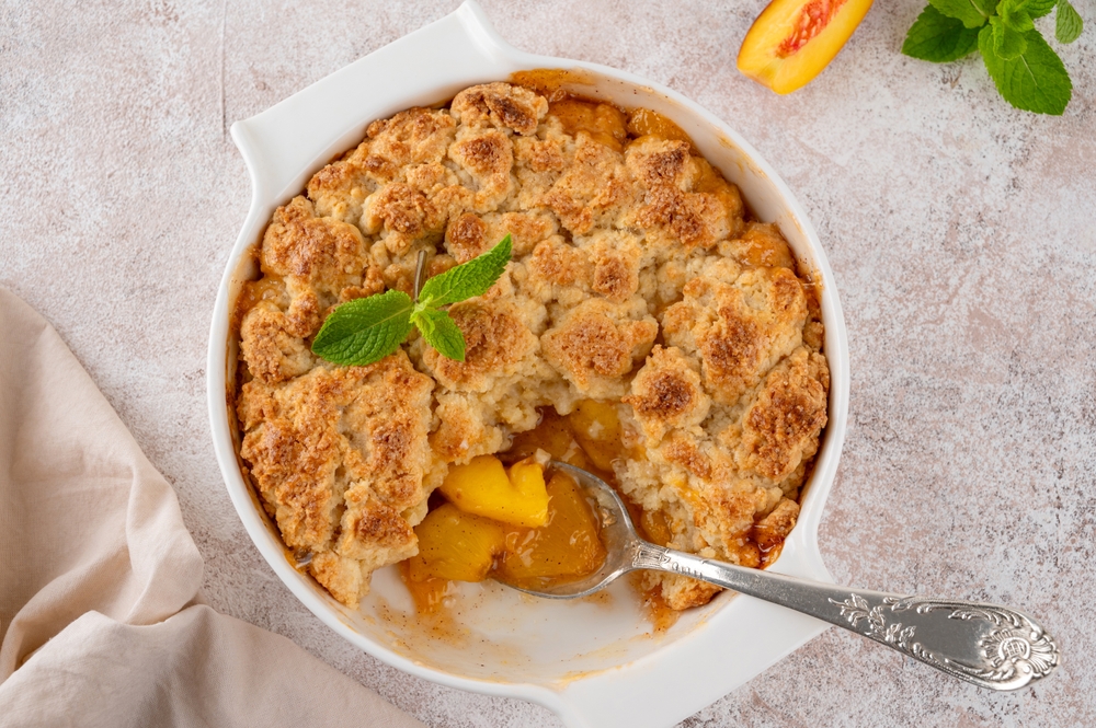 Homemade summer peach cobbler. Pie with juicy peaches, a scoop of vanilla ice cream and fresh mint on a white plate. Comfort food
