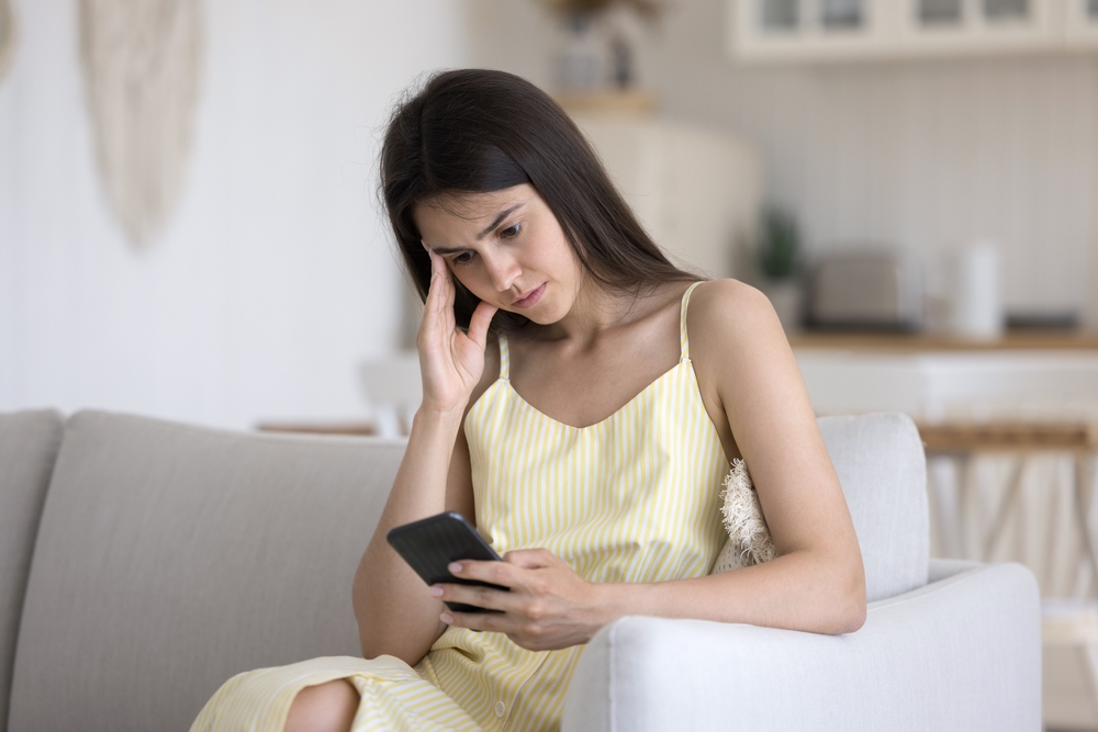 Stressed anxious young girl sit on sofa look on phone screen get bad news in email text read scam message deal with offensive comments on personal social media blog argue with boyfriend in online chat