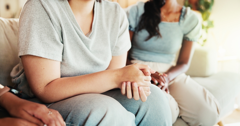 Women, hands or talking with discussion on sofa for care, support group or intervention at home. Closeup, female people or listening with friends on couch for confession, empathy or sympathy at house