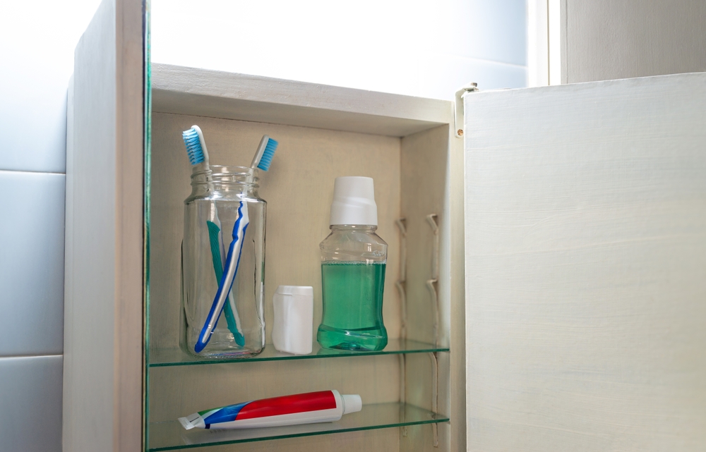 Oral hygiene items in bathroom medicine cabinet: toothbrush, dental floss, mouthwash, and toothpaste.