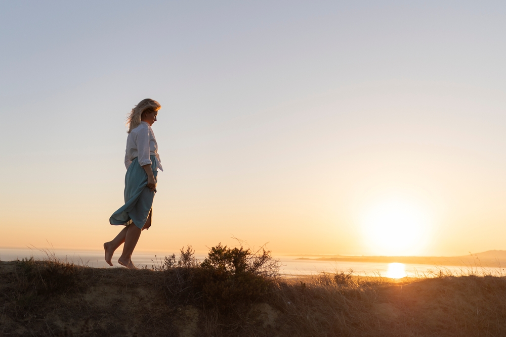 Woman walking barefoot on hilltop at sunset enjoying freedom and nature
