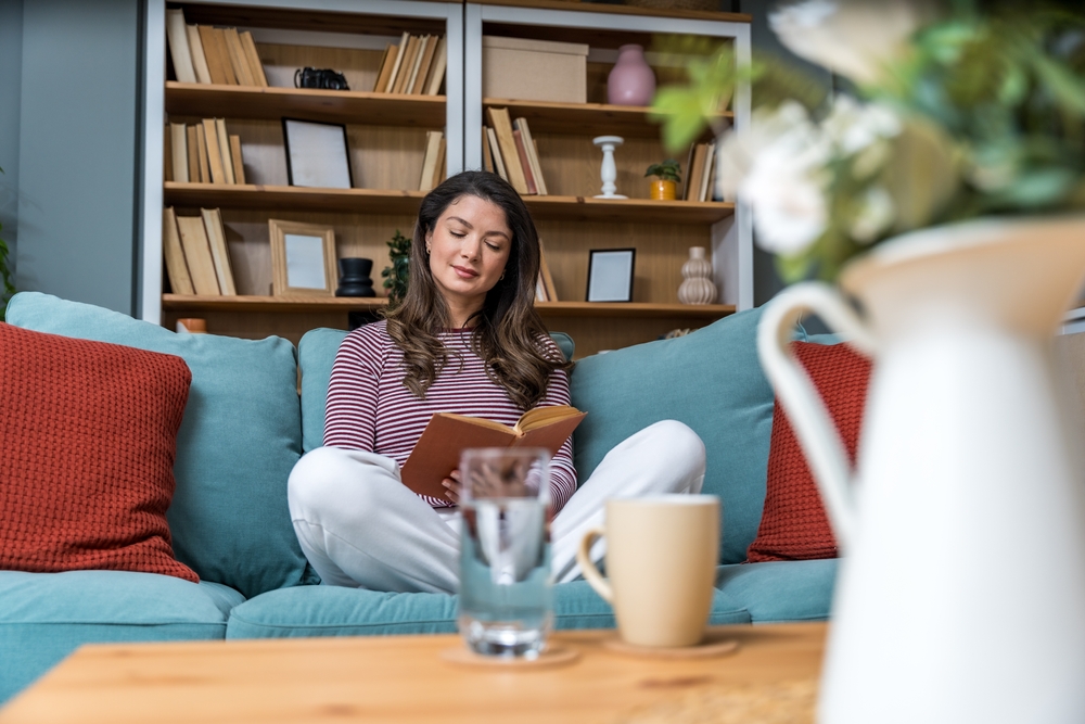 Young woman sitting at home reading a psychology book, working on herself and her mental health after a stressful situation. Female read book that her psychotherapist recommended to her after stress.