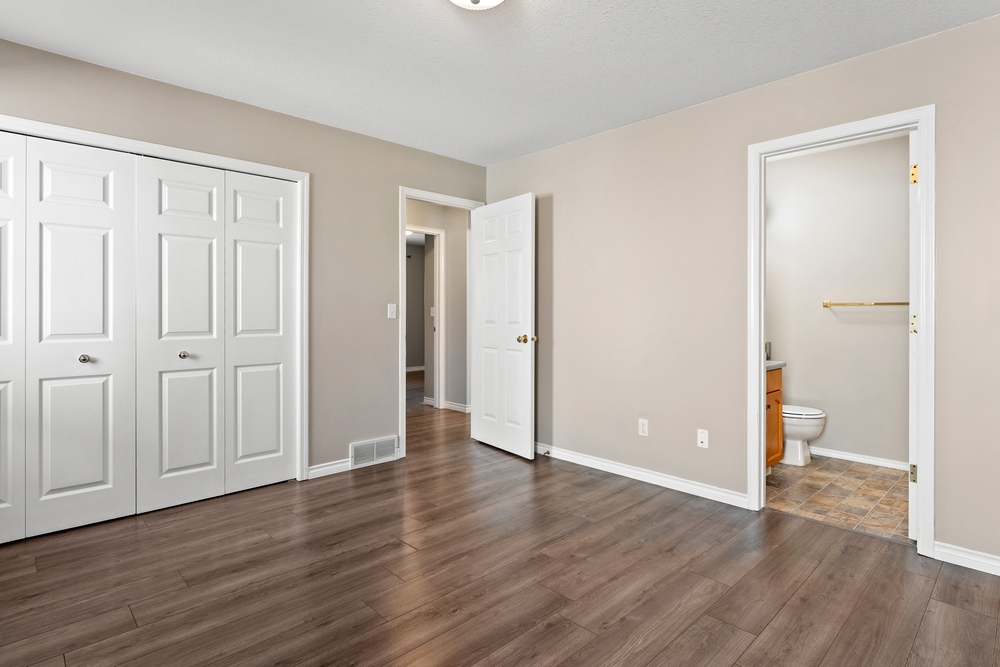 Large, empty bedroom with a white door and a white closet. The room is bare and uncluttered, with a wooden floor and a toilet in the corner