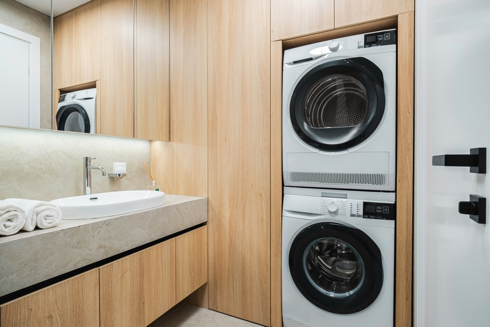 Bright laundry room features a stacked washer and dryer along with sleek wooden cabinetry and a modern sink, creating an efficient and stylish space for household chores