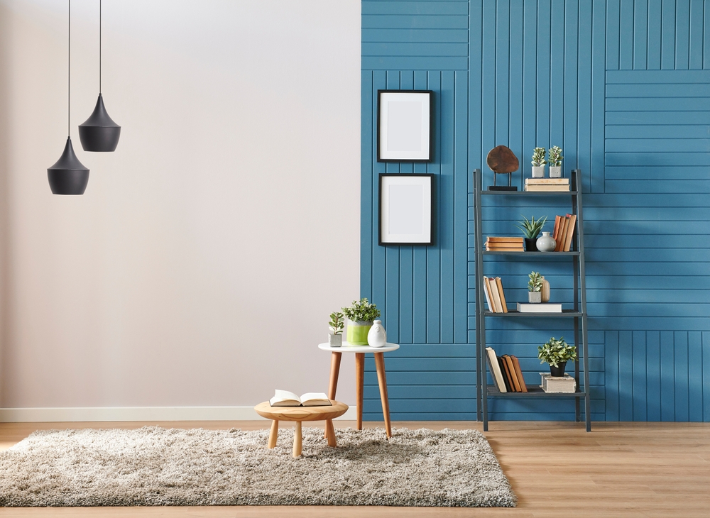 Stylish modern interior with blue accent wall, bookshelf decor, small tables, indoor plants, cozy rug, and minimalist design creating a comfortable and aesthetic home atmosphere.