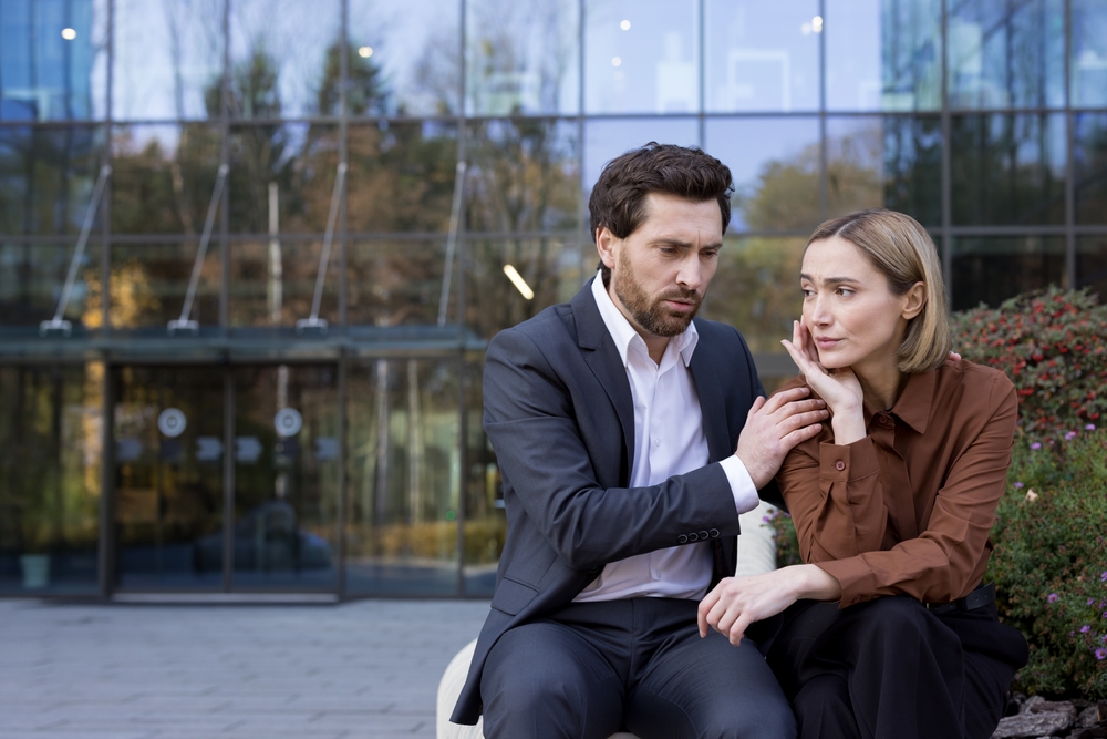 Business colleagues experiencing a difficult moment together, the empathetic man offering support to the upset woman with a hand on her shoulder during a hard conversation or delivering bad news