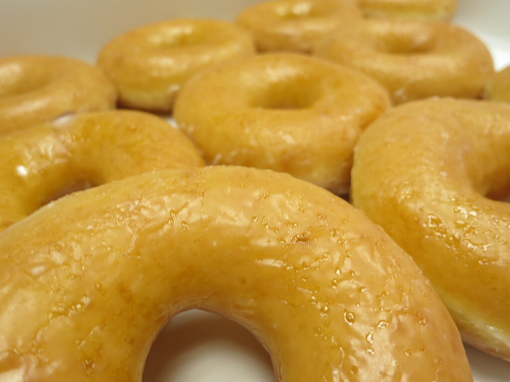 Golden glazed ring doughnuts with a shiny sugar coating, one with a bite taken out of it.