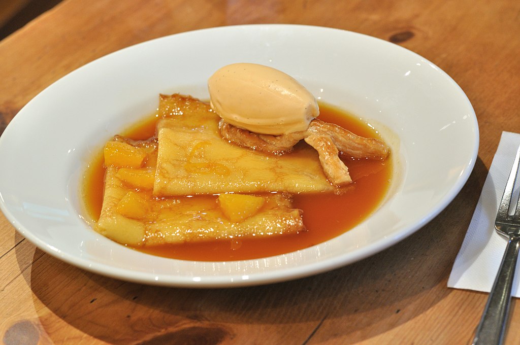 Crepes suzette in orange sauce topped with a scoop of ice cream.