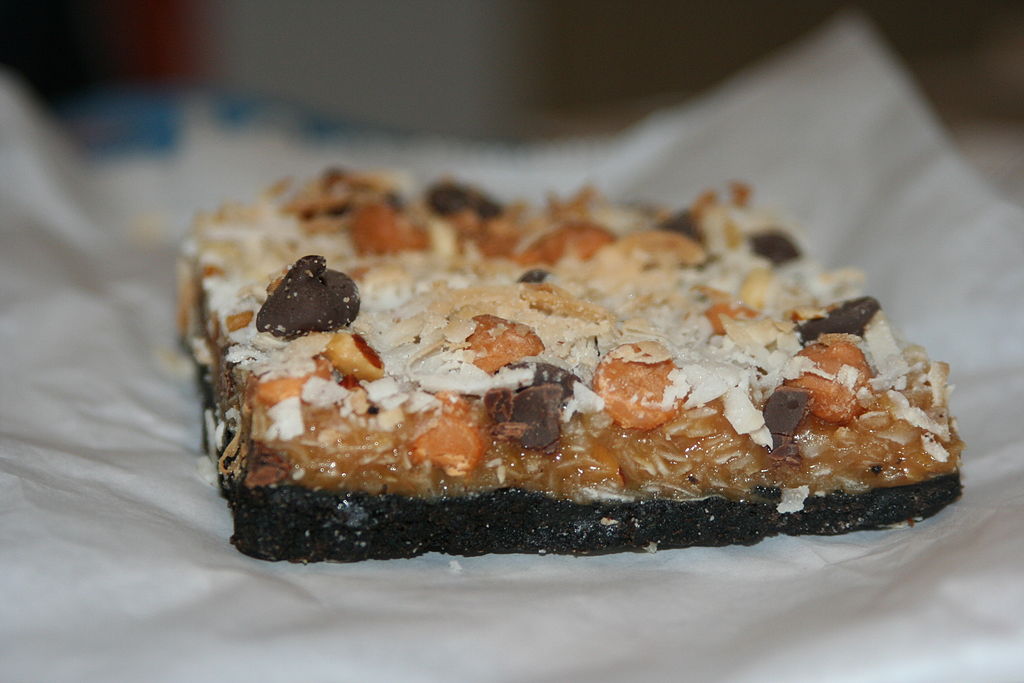 A layered cookie bar showing chocolate chips, shredded coconut and butterscotch chips on a chocolate cookie base.