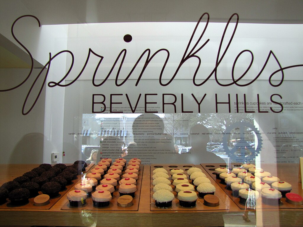 The Sprinkles Beverly Hills bakery window displaying rows of cupcakes in chocolate, vanilla and pastel flavors.