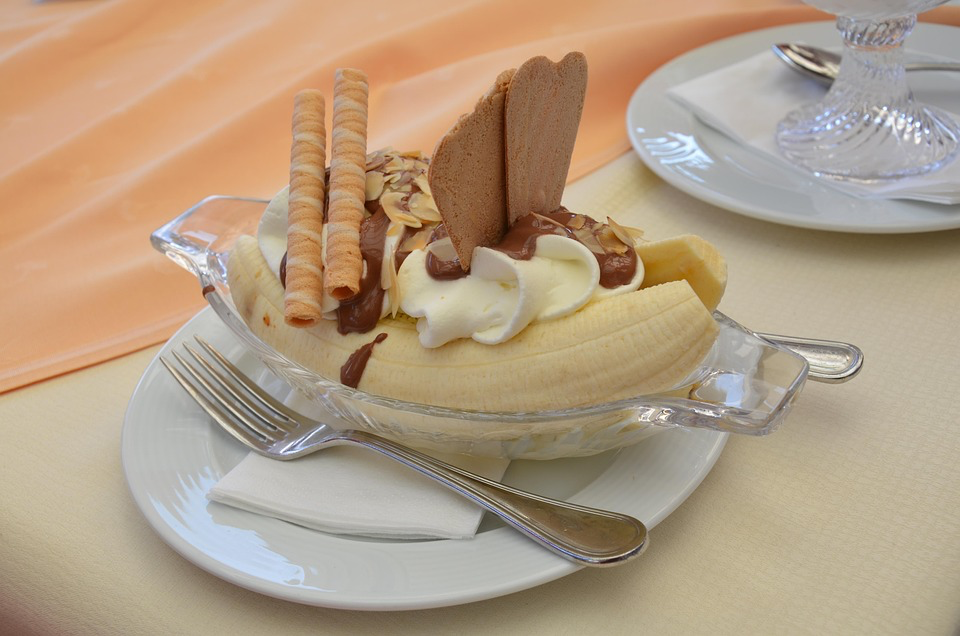 Banana split in a glass dish with ice cream, chocolate sauce, and wafer cookies.