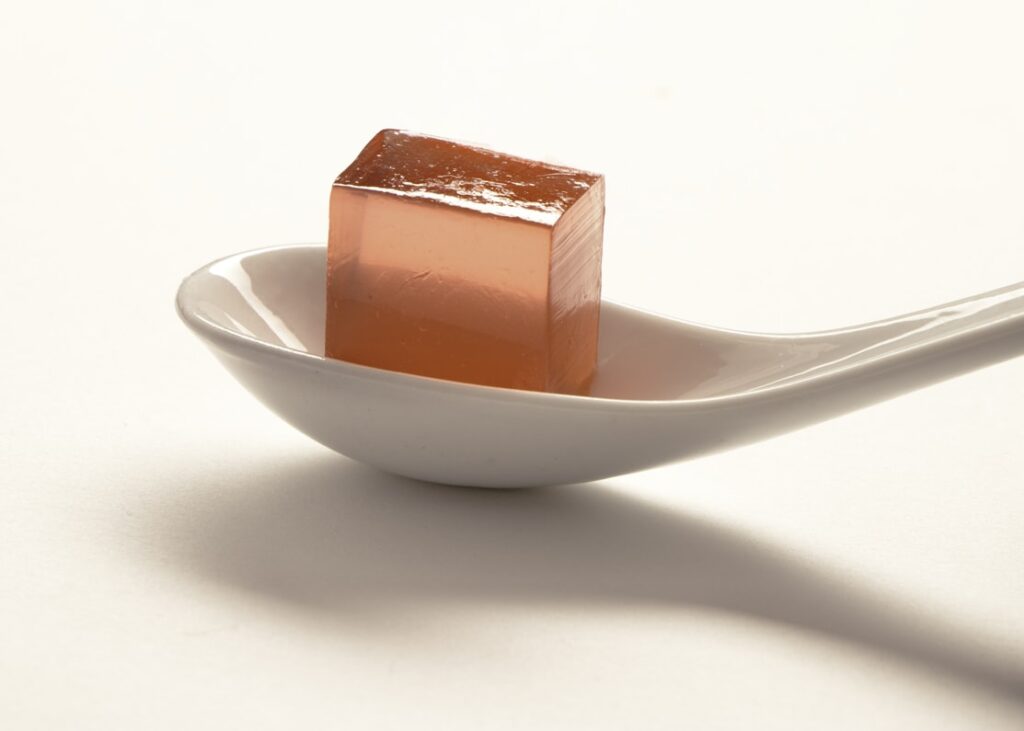 Cube of red gelatin balanced on a white spoon.