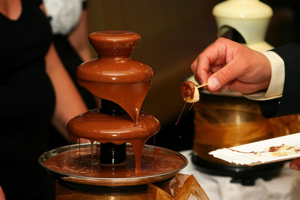 Chocolate fountain with a hand dipping food into the flowing chocolate.