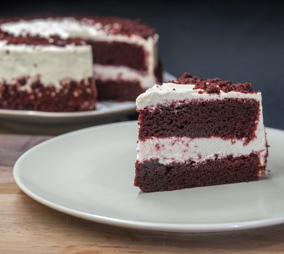Red velvet cake with cream cheese frosting, slice plated in foreground.