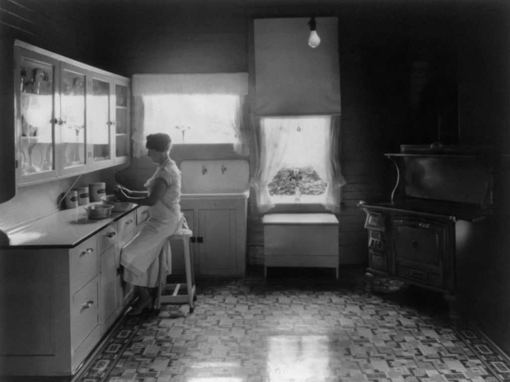 Black and white photo of a woman working in an early 1900s kitchen.