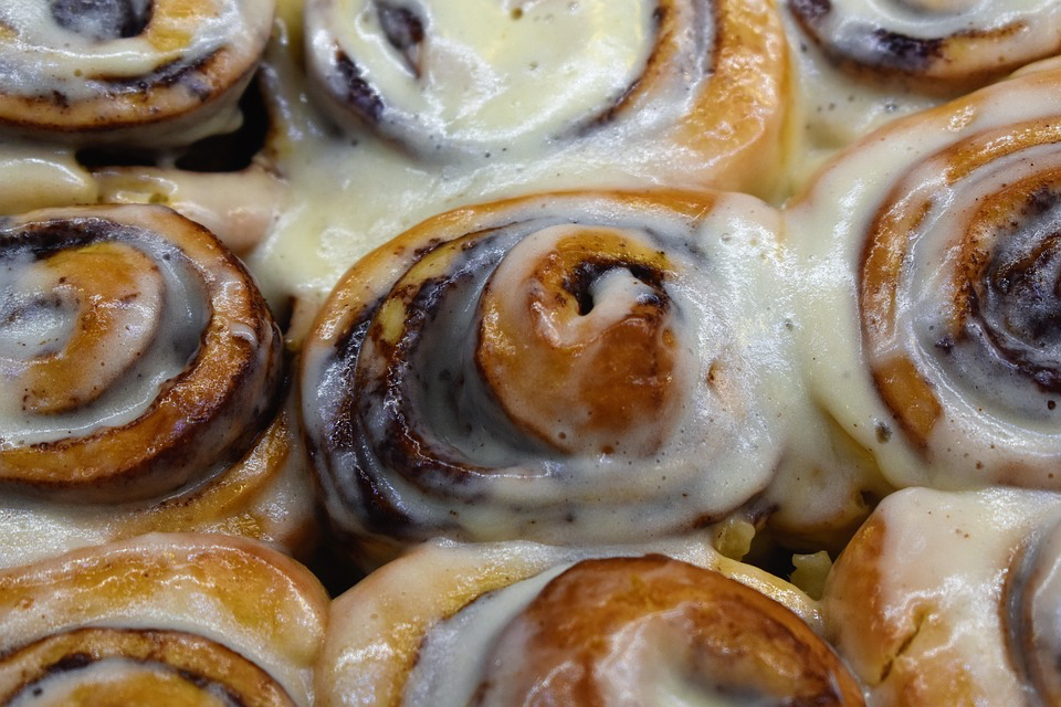 Close-up of freshly baked cinnamon rolls with cream cheese frosting pooling between the swirled layers.