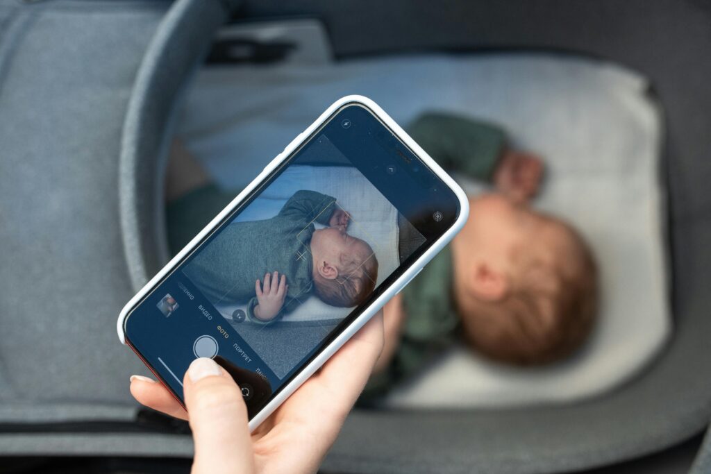 A woman holds her smartphone to take a photo of her baby sleeping in a bassinet.