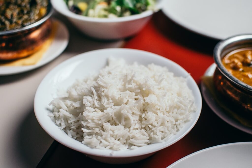 Bowl of fluffy white basmati rice alongside dishes of curry and salad on a restaurant table.