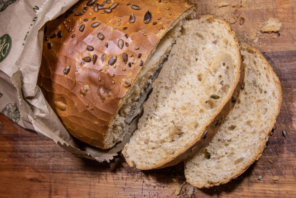 Rustic seeded bread loaf partially sliced on wooden cutting board, showing soft interior with seeds throughout.