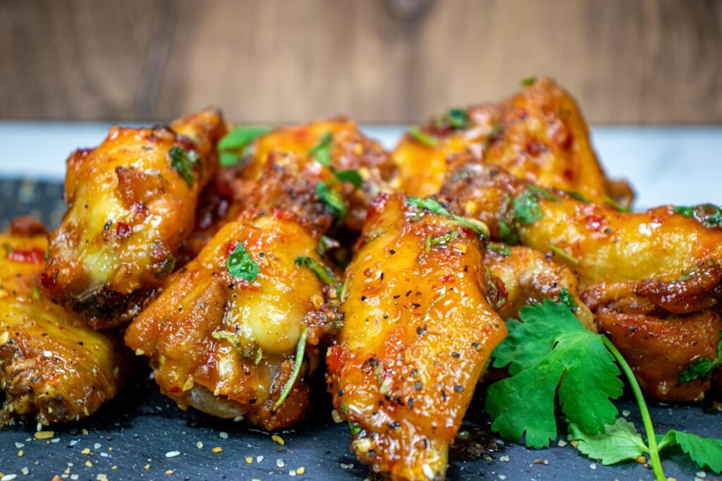 Glazed chicken wings with herbs, black pepper, and red pepper flakes, garnished with fresh cilantro on dark slate surface.