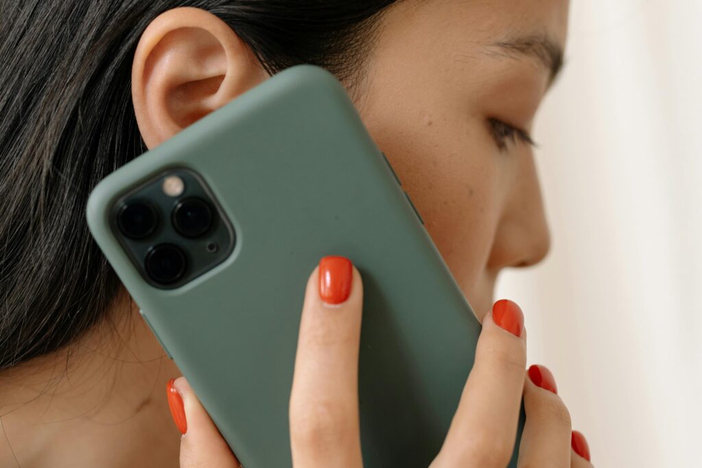 Woman with dark hair and red nail polish holding a smartphone to her ear, shown in profile.