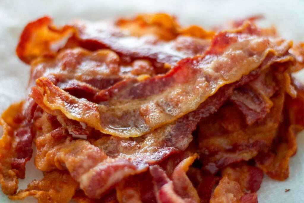 Stack of crispy cooked bacon strips with glistening fat, resting on parchment paper.